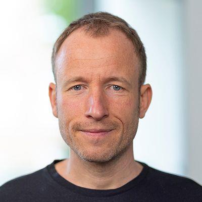 Porträt von Danilo Ziemen mit leichtem Lächeln vor hellem, unscharfem Hintergrund in einem Innenraum
